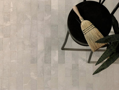 A natural-bristle broom with a light wood handle resting on a black chair in a natural stone tiles collection