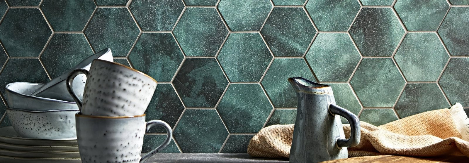 Stoneware ceramic mugs with speckled gray and white glaze stacked beside a matching pitcher on rustic wood surface nebula tiles