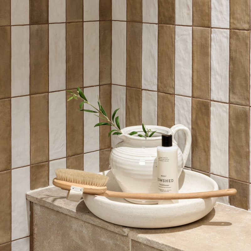 White ceramic pitcher with handle holding greenery beside brody lowshed conditioner bottle on white basin from oasis ceramic