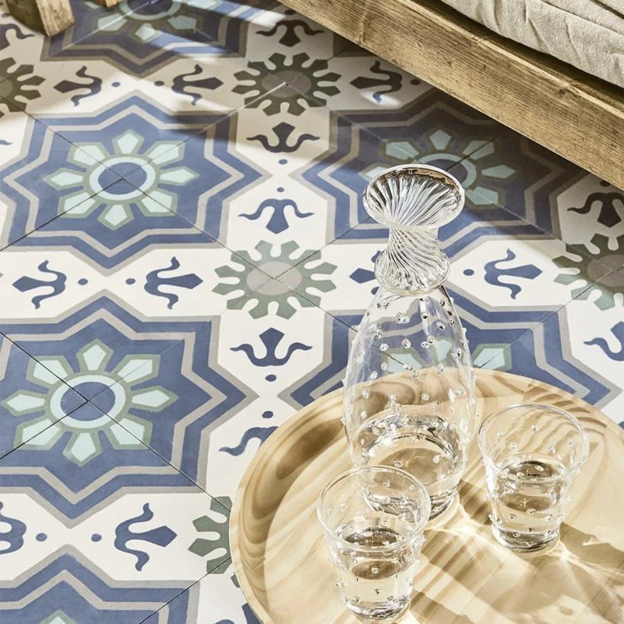 Clear glass decanter with fluted scalloped stopper and textured body on wooden tray with two matching glasses on encaustic tiles