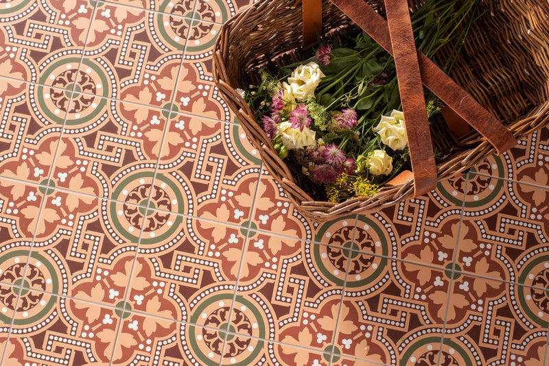 A woven wicker basket with brown leather straps filled with white and purple flowers on patterned floor tiles