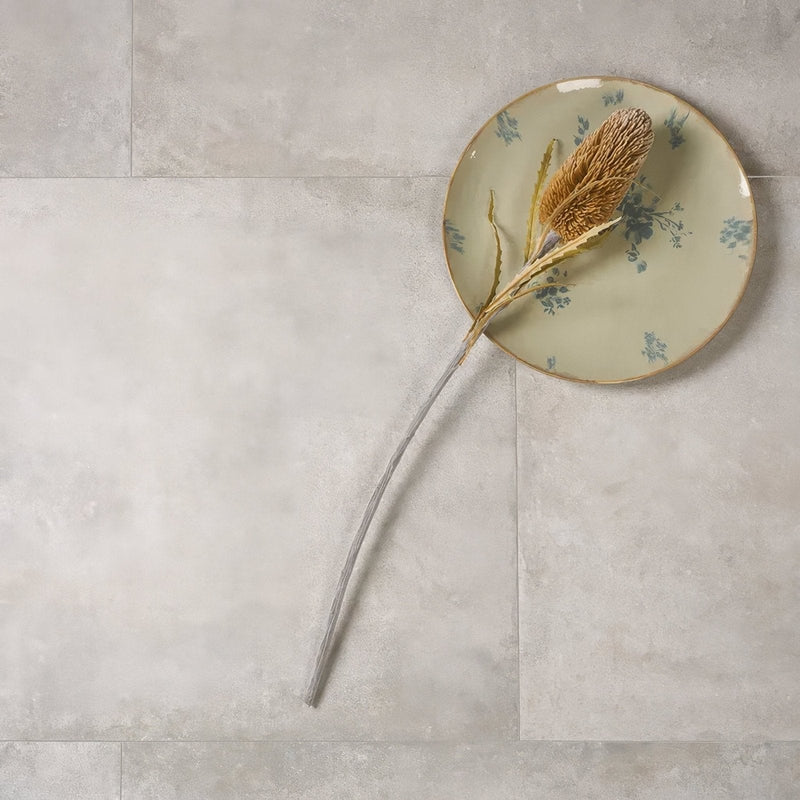 A dried golden-brown flower with a long slender stem on an off-white Pierre Porcelain plate with blue floral patterns