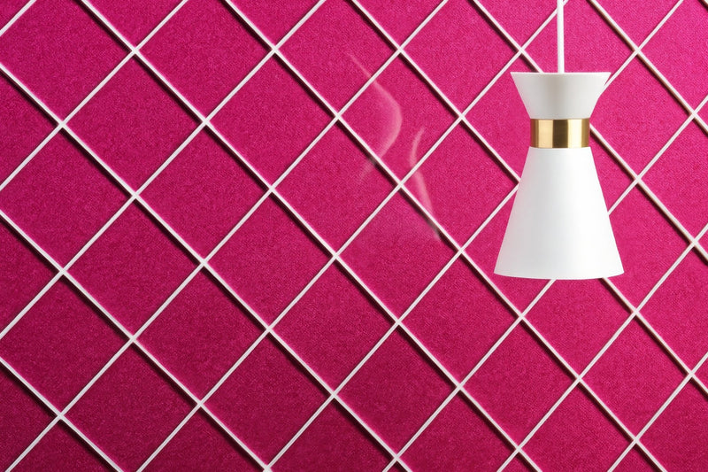 A sleek white pendant lamp with a gold accent band hangs against a vibrant magenta textured wall in a pink bathroom tiles collection.