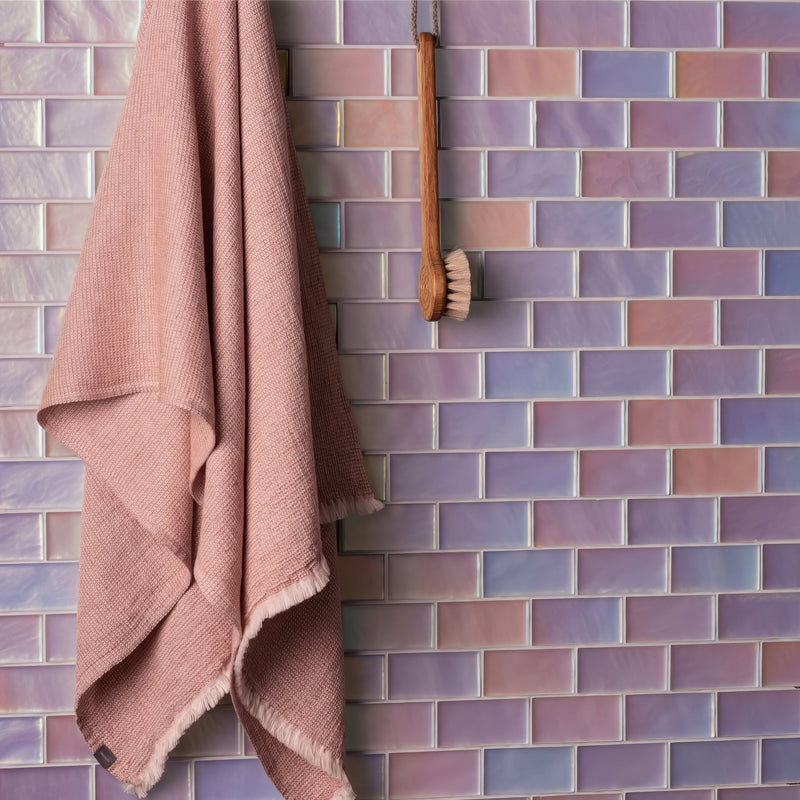 A soft pink textured towel with frayed edges hangs against iridescent purple and pink mosaic tiles background