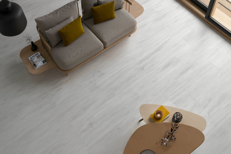 Modern gray sofa with mustard yellow throw pillows and light wood frame showcased on plank floor tiles collection.