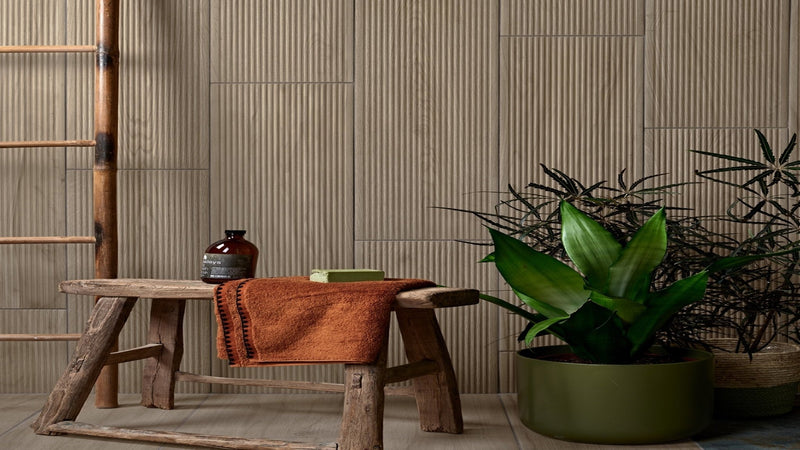 Rustic wooden bench with textured orange towel and dark brown ceramic jar beside it in plank wall tiles collection.