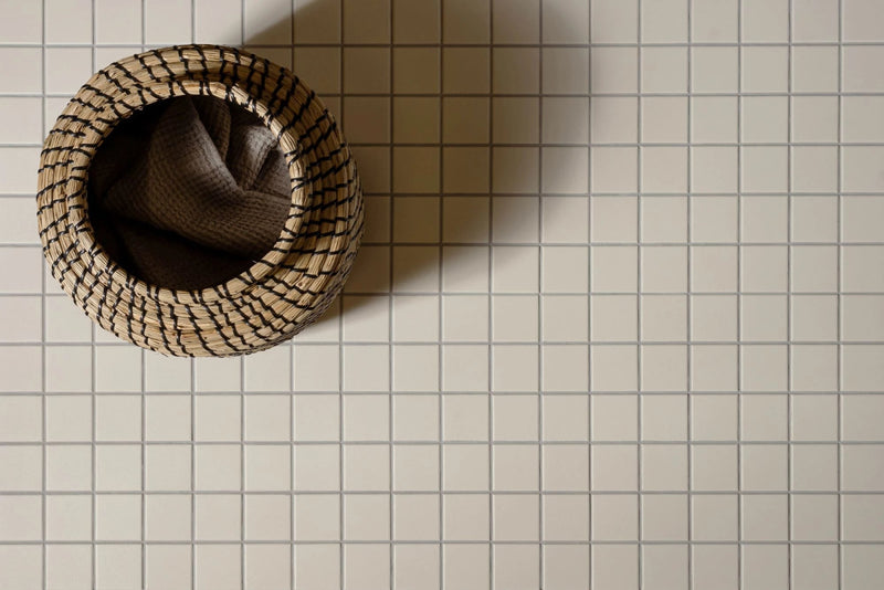 Handwoven beige and dark brown basket with textured interlaced pattern featured in porcelain mosaic tiles collection.