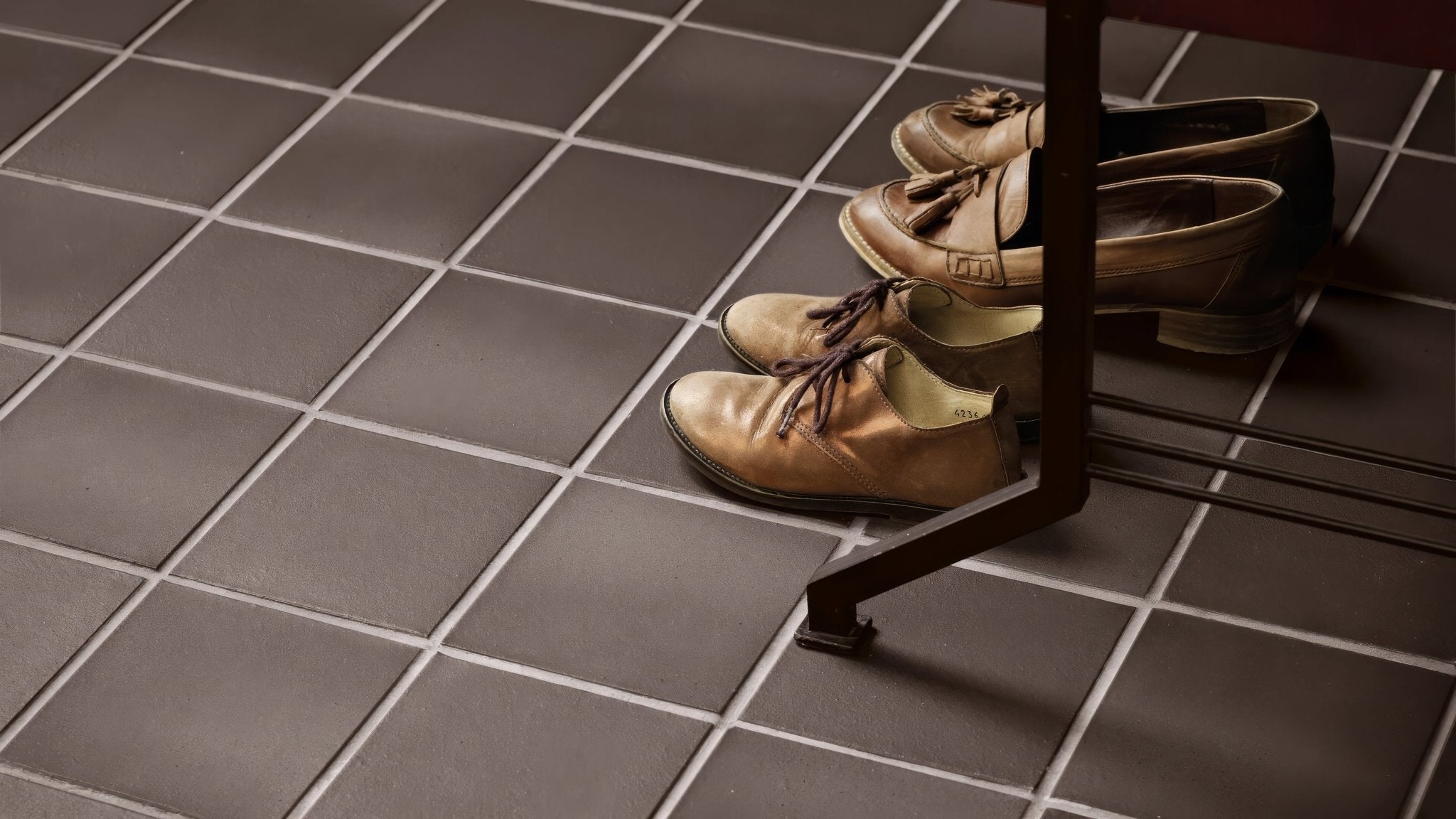 A pair of tan leather lace-up oxford shoes with dark brown laces resting on quarry bathroom tiles under a table leg