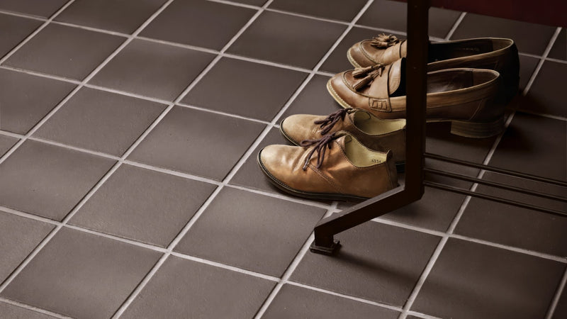 A pair of tan leather lace-up oxford shoes with dark brown laces resting on quarry bathroom tiles under a table leg