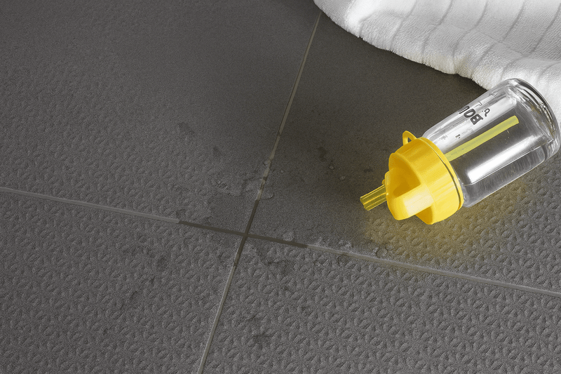 A transparent plastic baby bottle with a bright yellow cap and measurement markings in a quarry floor tiles collection
