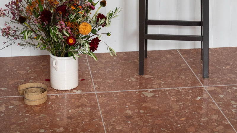 A white ceramic vase filled with vibrant autumnal flowers displayed on red floor tiles