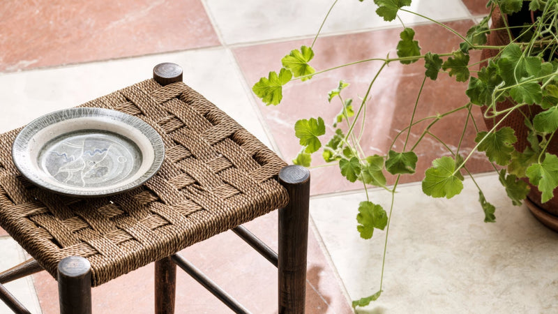 A woven brown rope stool with dark wooden legs holding a ceramic plate with gray and white intricate patterns