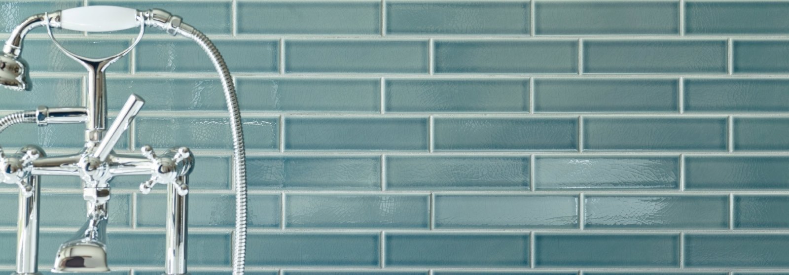 Chrome-finished brass faucet with curved spout and separate hot and cold handles mounted on teal retro metro tiles