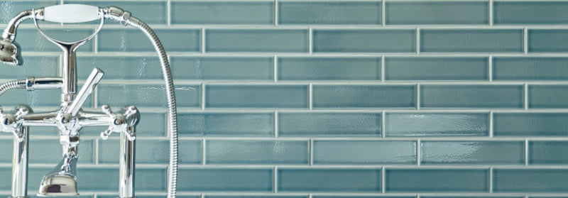 Chrome-finished brass faucet with curved spout and separate hot and cold handles mounted on teal retro metro tiles