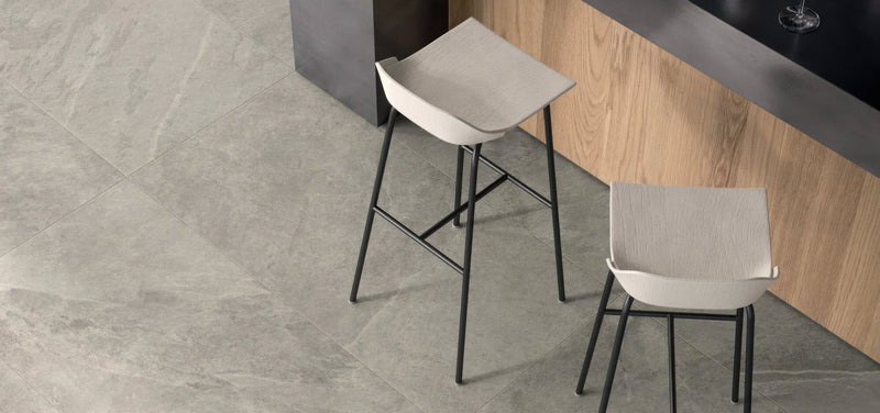 Modern minimalist bar stools with sleek black metal frames and light gray upholstered seats in slate effect porcelain tiles collection