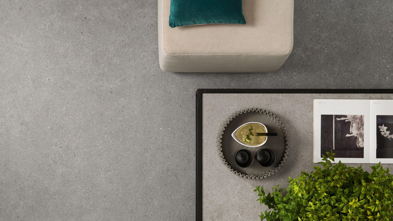 A teal velvet cushion resting on a beige upholstered ottoman in a stone effect kitchen tiles collection