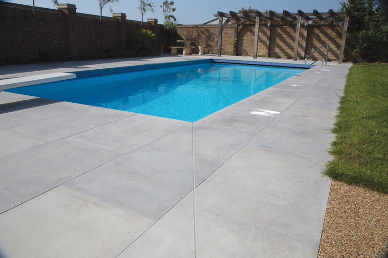 Rectangular swimming pool floor tiles with vibrant blue surface bordered by light gray concrete and green grass