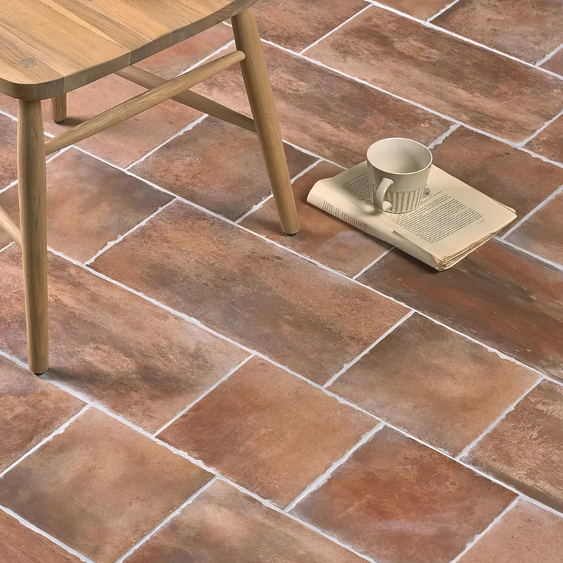 Beige ceramic mug with vertical ridged texture resting on open book on terracotta effect tiles floor.