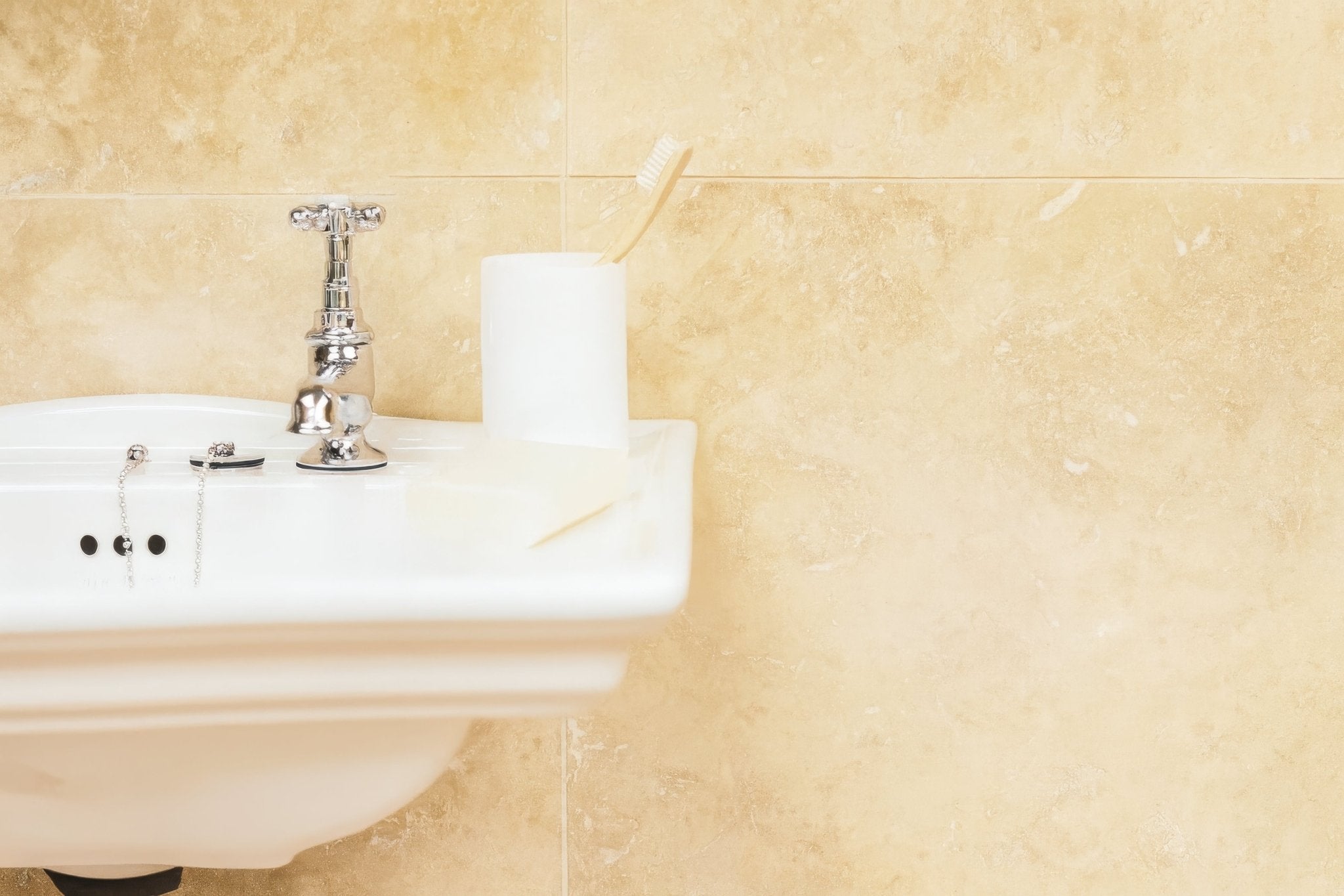 White ceramic bathroom sink with polished chrome faucet and chain-style handles in travertine bathroom tiles collection