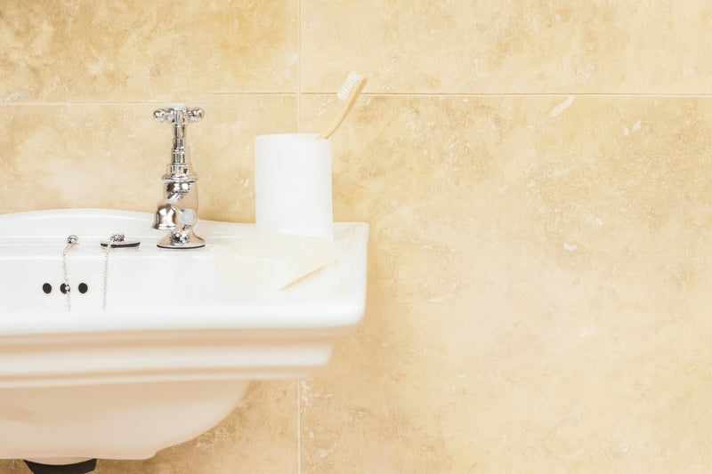 White ceramic bathroom sink with polished chrome faucet and chain-style handles in travertine bathroom tiles collection