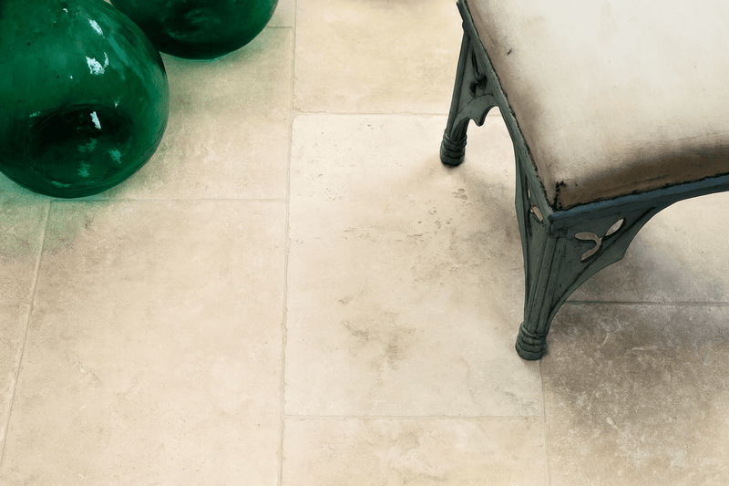 Dark green glass vase with rounded bulbous shape and glossy finish displayed with travertine floor tiles