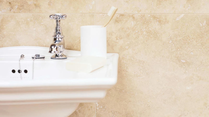 White ceramic bathroom sink with polished chrome faucet and drain stopper in travertine wall tiles collection