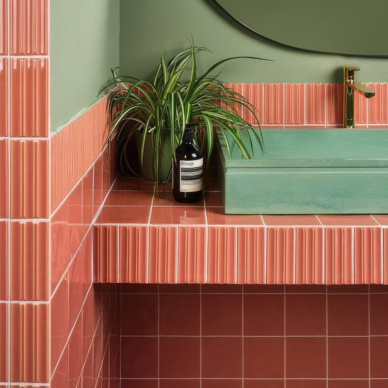 A sleek matte black aesop shower gel bottle with a minimalist label on a coral tiled countertop from tunstall ceramic