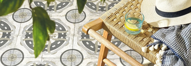 A light beige straw hat with a black ribbon band resting on a woven wicker chair from urban tiles collection