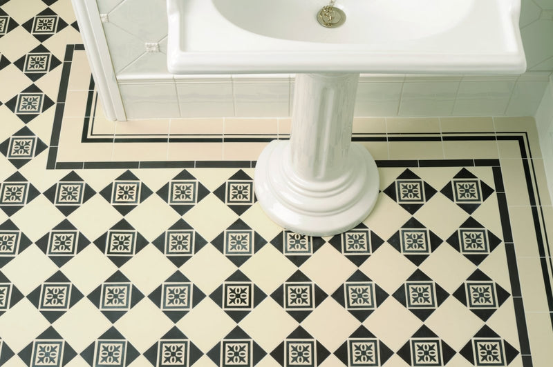 White ceramic pedestal sink with classic fluted base and circular chrome faucet in victorian floor tile borders collection