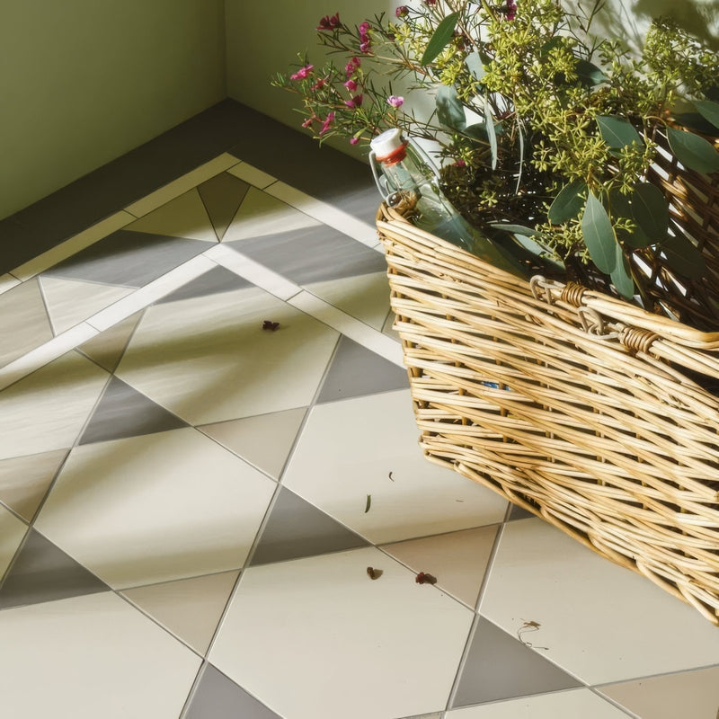 A woven wicker basket with greenery pink flowers and a glass bottle in the victorian floor tiles hexham pattern collection