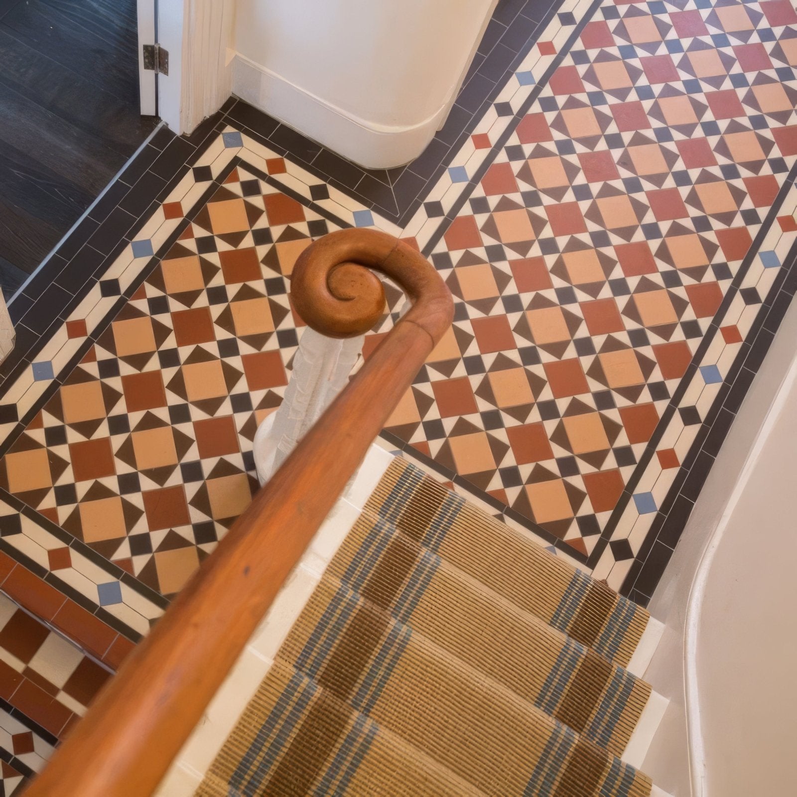 A polished wooden staircase handrail with a curved spiral top in victorian floor tiles lambeth pattern collection