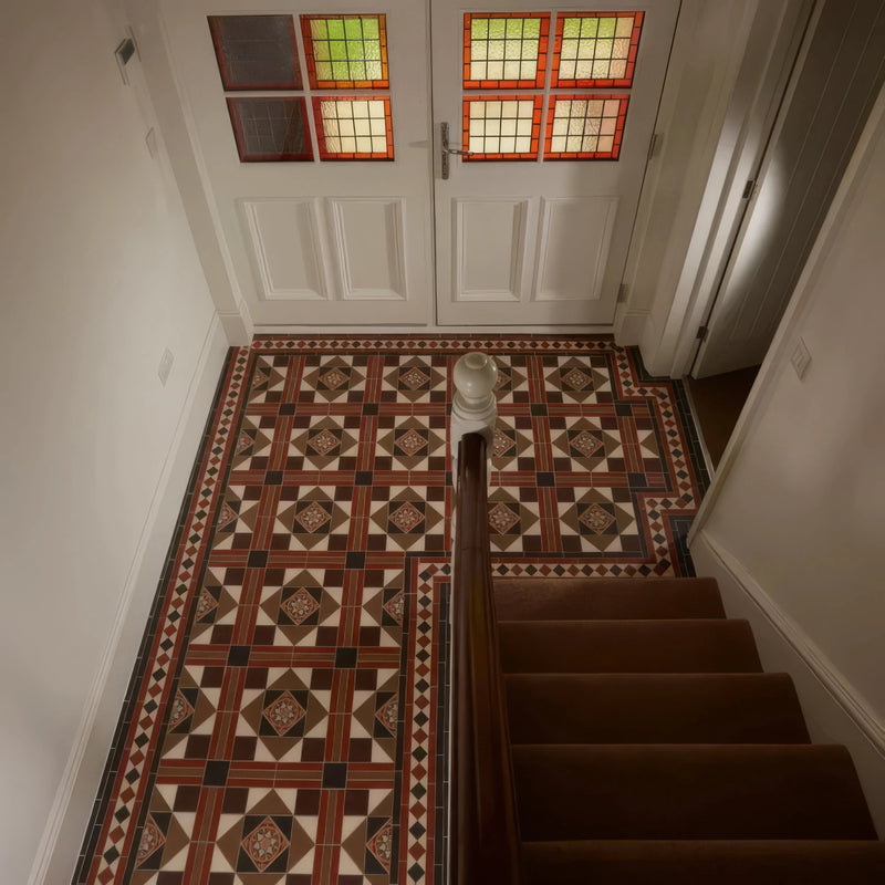 A staircase with dark brown wooden steps and handrail leading to white double doors with stained glass in victorian floor tiles lindisfarne pattern