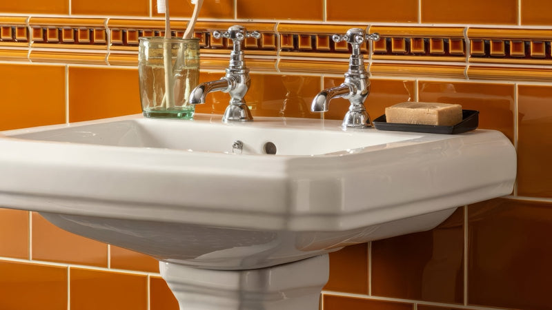 White ceramic pedestal sink with two chrome faucets in a victorian wall tiles collection