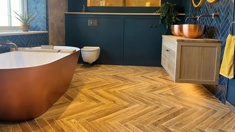 Copper freestanding bathtub with smooth reflective surface and rounded edges in wood effect bathroom tiles collection