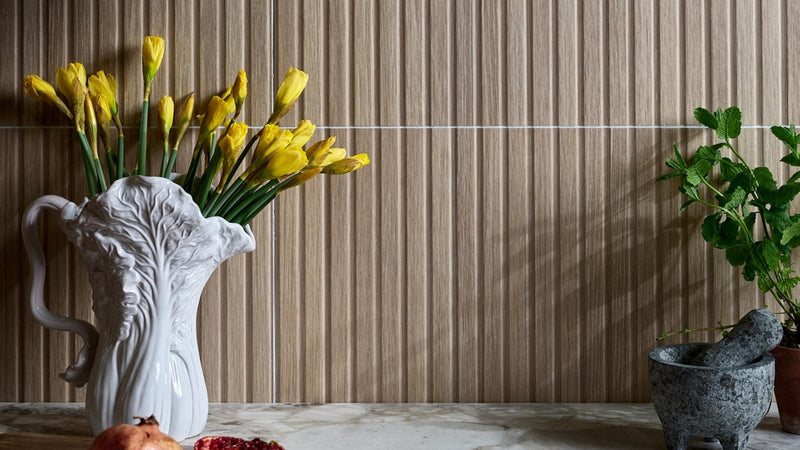 White ceramic vase shaped like a cabbage with yellow daffodils on a wood effect wall tile background