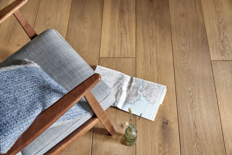 Gray upholstered chair with wooden frame and blue textured throw blanket in woodpecker chepstow flooring collection
