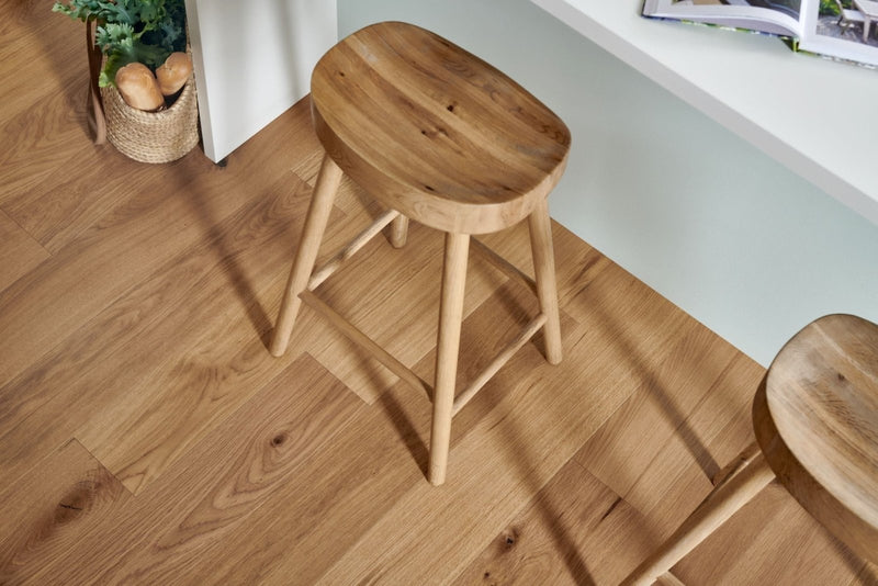 A light wood stool with a rounded seat and four slender legs displayed on woodpecker highclere herringbone engineered flooring