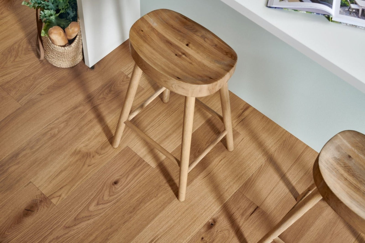 A light wood stool with a rounded seat and four slender legs displayed on woodpecker highclere herringbone engineered flooring