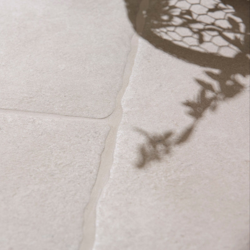 A delicate dark brown lace shadow cast on textured white porcelain tile from wychwood porcelain and limestone collection