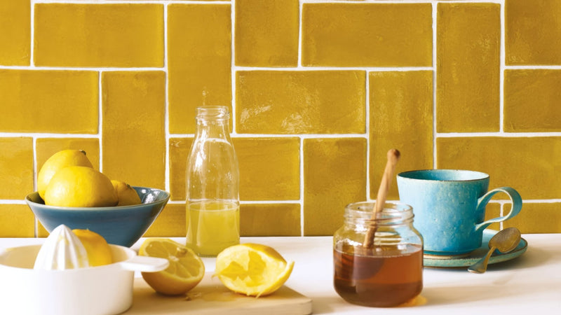 A blue ceramic mug with textured surface on a matching saucer beside a honey jar and wooden spoon in yellow kitchen tiles