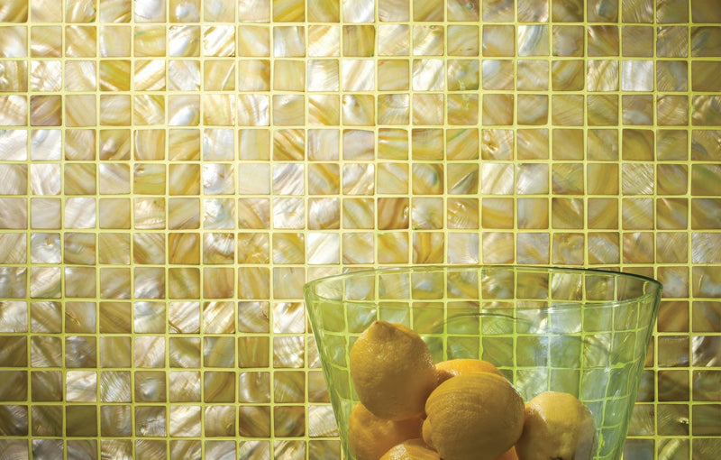 A translucent green glass bowl filled with lemons in a yellow mosaic tiles collection