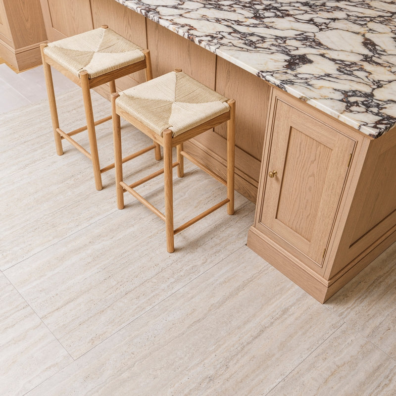 Two light wood bar stools with woven beige rope seats beside a marble countertop in the zahara porcelain collection