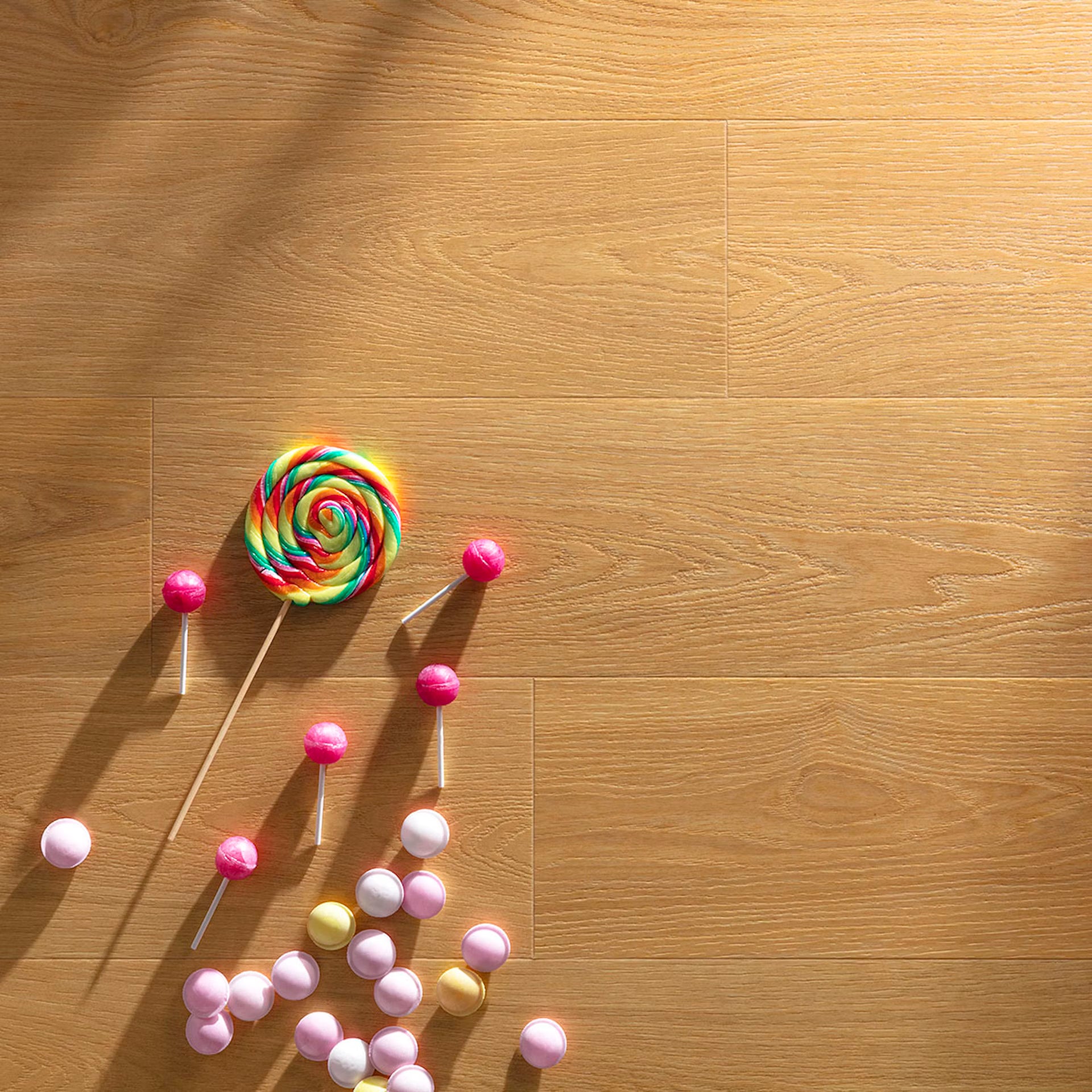 A vibrant rainbow lollipop on honey F025 long vinyl planks with warm-toned wood grain and scattered colorful candies