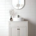 Bathroom vanity with round mirror, sink, and decorative vase on a tiled wall.