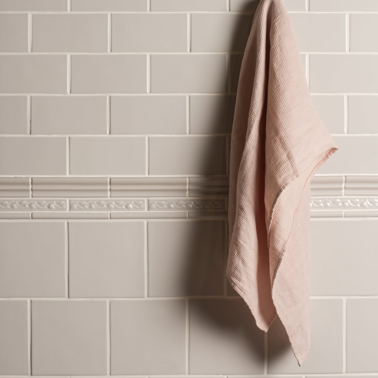 A soft blush pink linen towel with textured weave hanging on white subway tiles from beaulieu moulding waveney