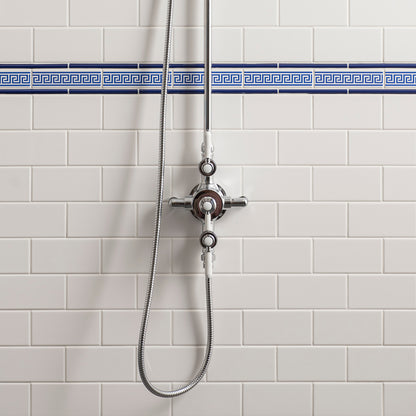 A chrome shower valve and handheld shower head mounted on a white subway tile wall with a blue Greek key border stripe.