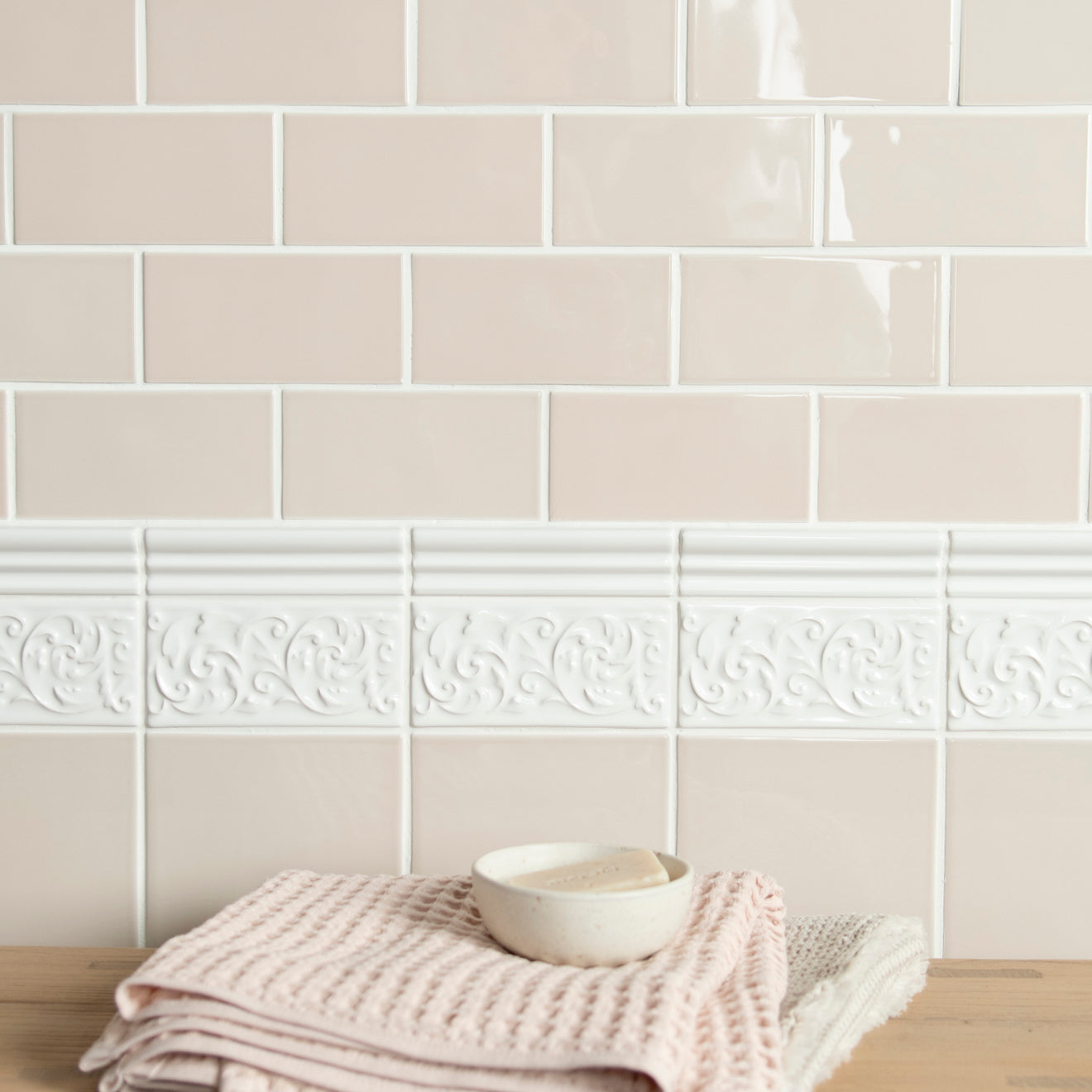 Beige tiles with decorative border and folded towel on wooden surface