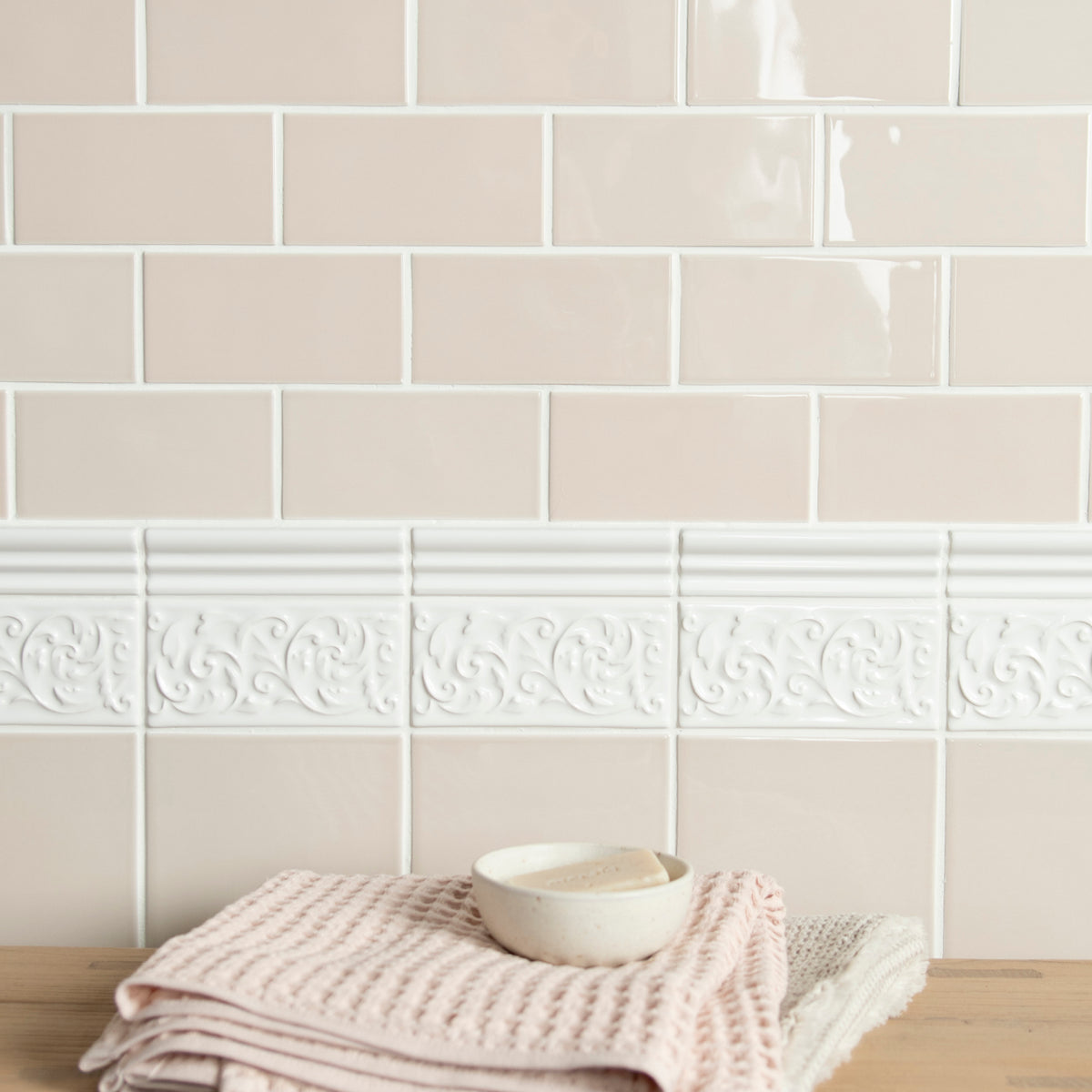 Beige tiles with decorative border and folded towel on wooden surface