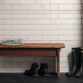 Wooden bench with folded clothes against a tiled wall, with boots and rain boots on the floor.