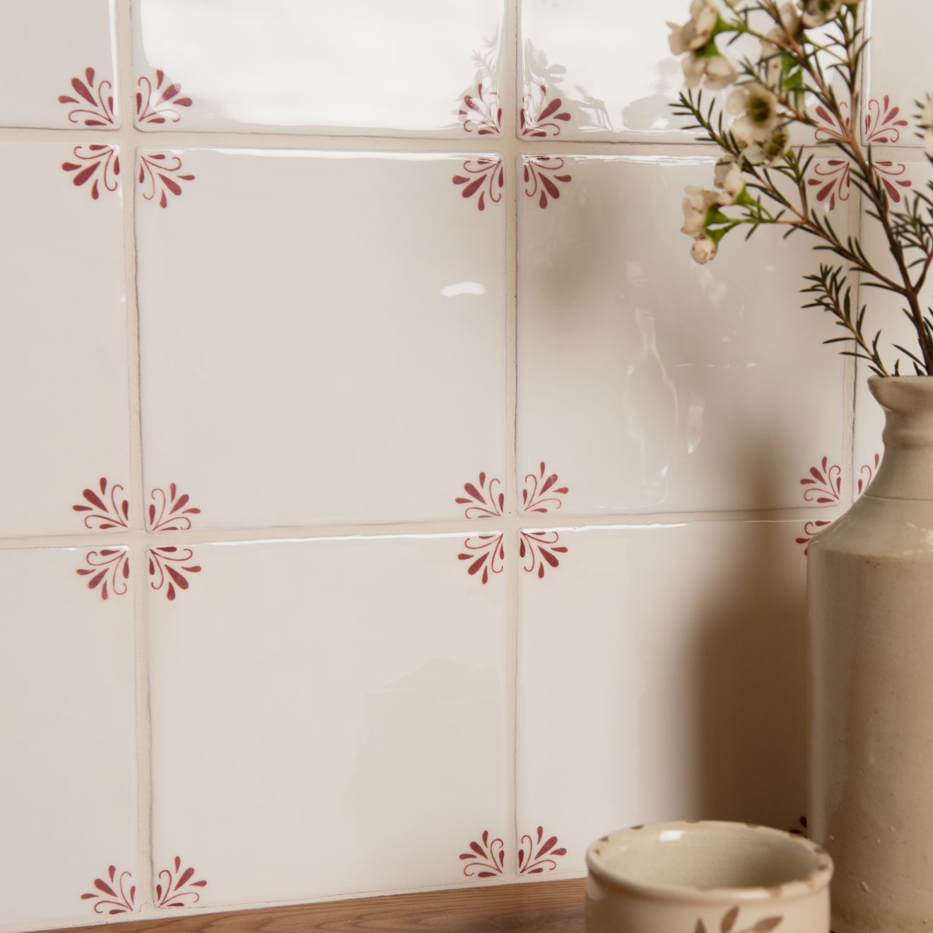 Decorative tiles with floral patterns on a wall next to a vase and small bowl.